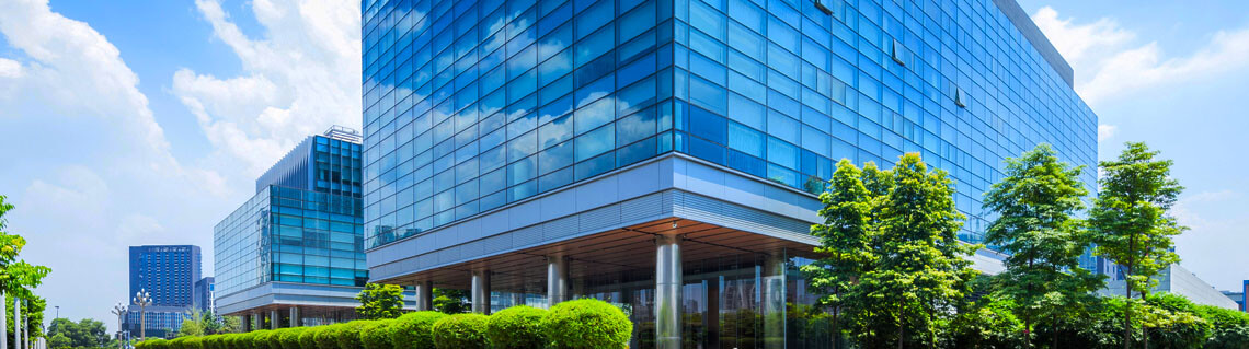 Exterior view of a commercial all glass office building with green trees surrounding it